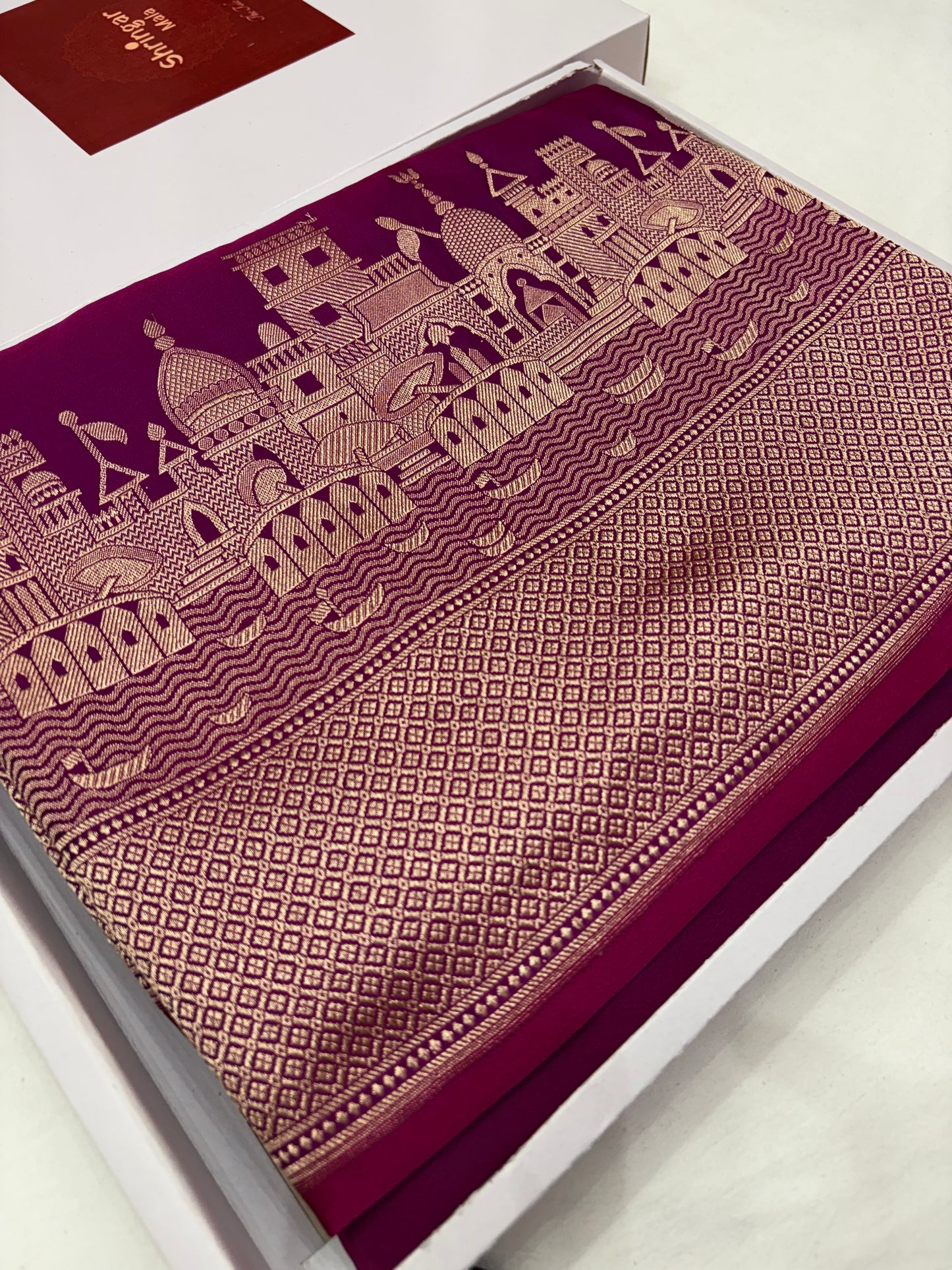 Maroon fabric with gold architectural design on a white box