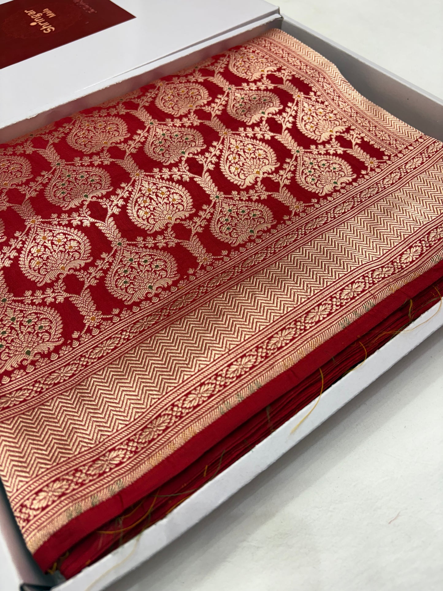 Red fabric with intricate gold patterns on a white surface