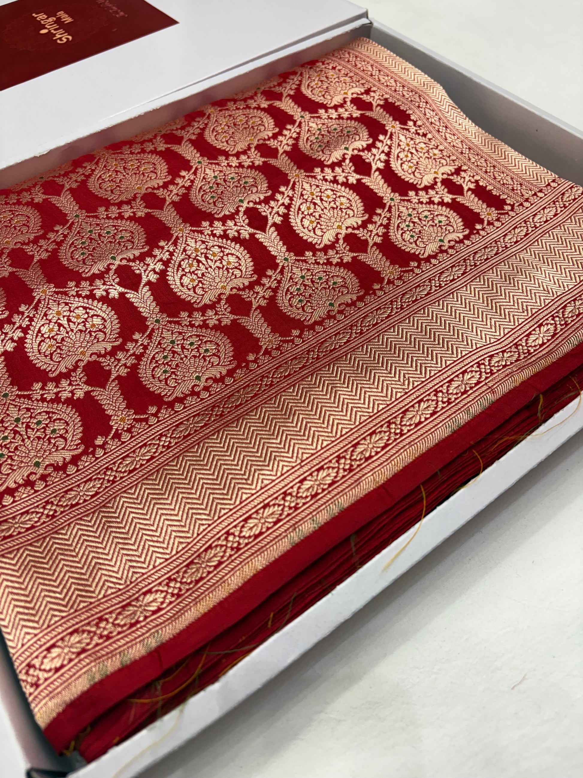 Red fabric with intricate gold patterns on a white surface