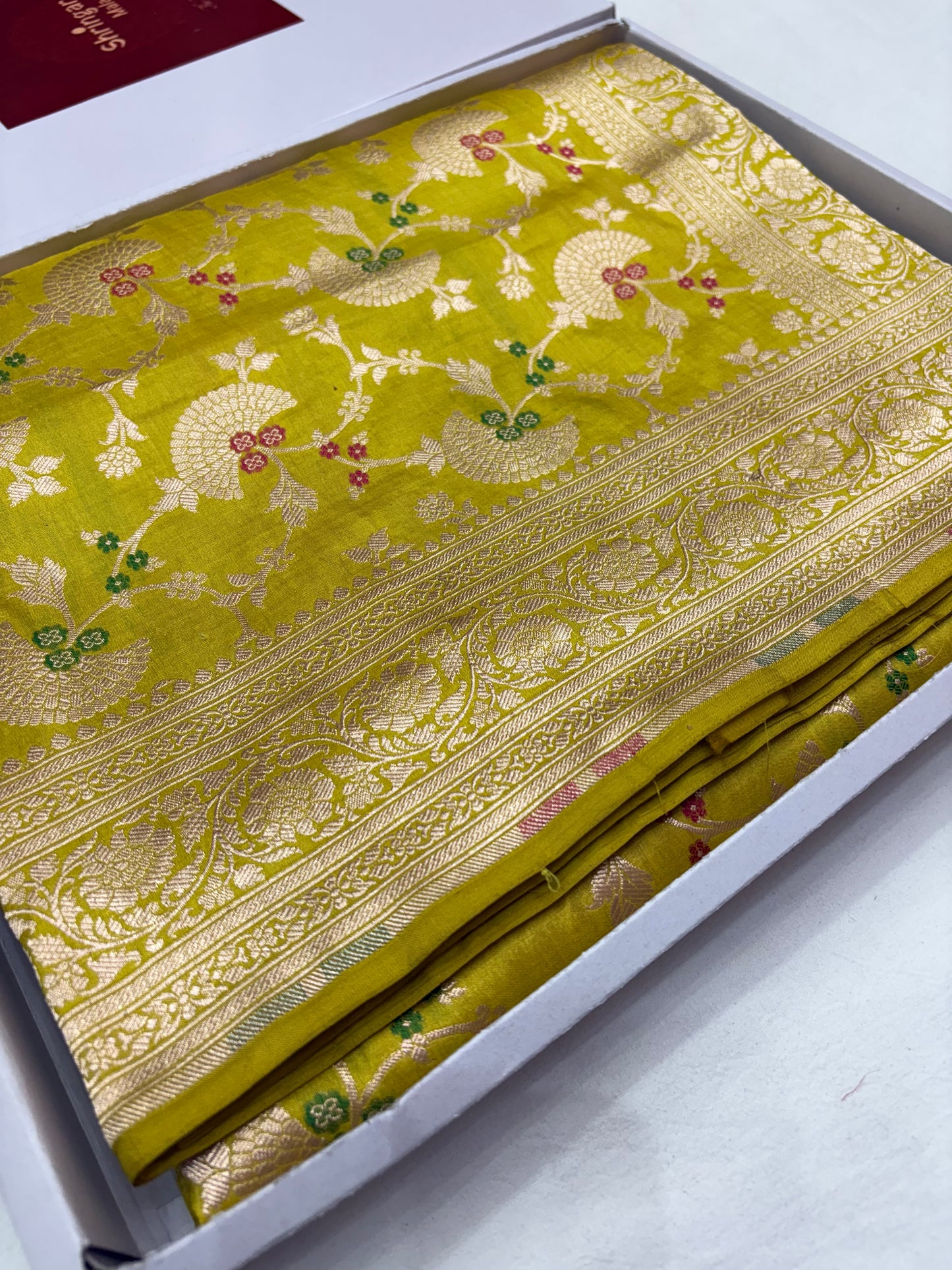 Green fabric with gold embroidery in a box on a white background